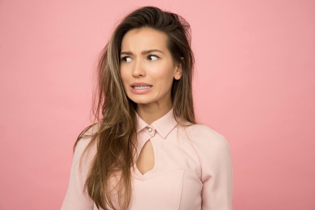 A young woman with a playful uncertain expression against a pink background.