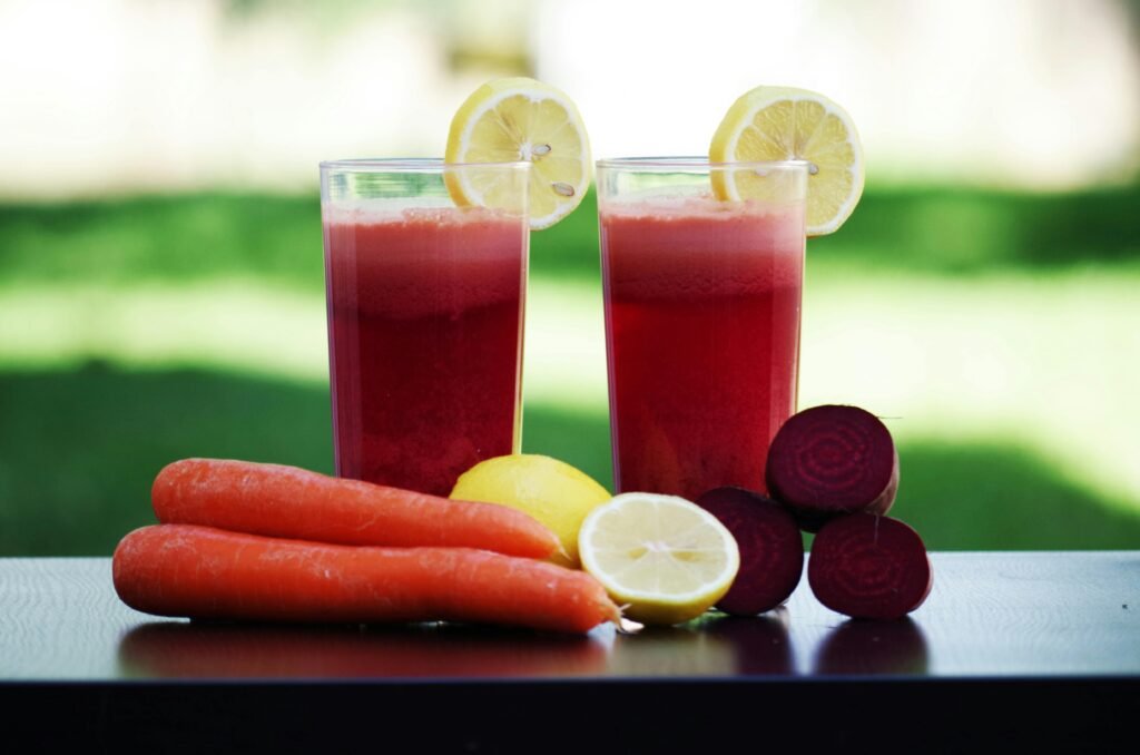 Colorful glasses of beetroot and carrot juice garnished with lemon slices, symbolizing health and freshness.