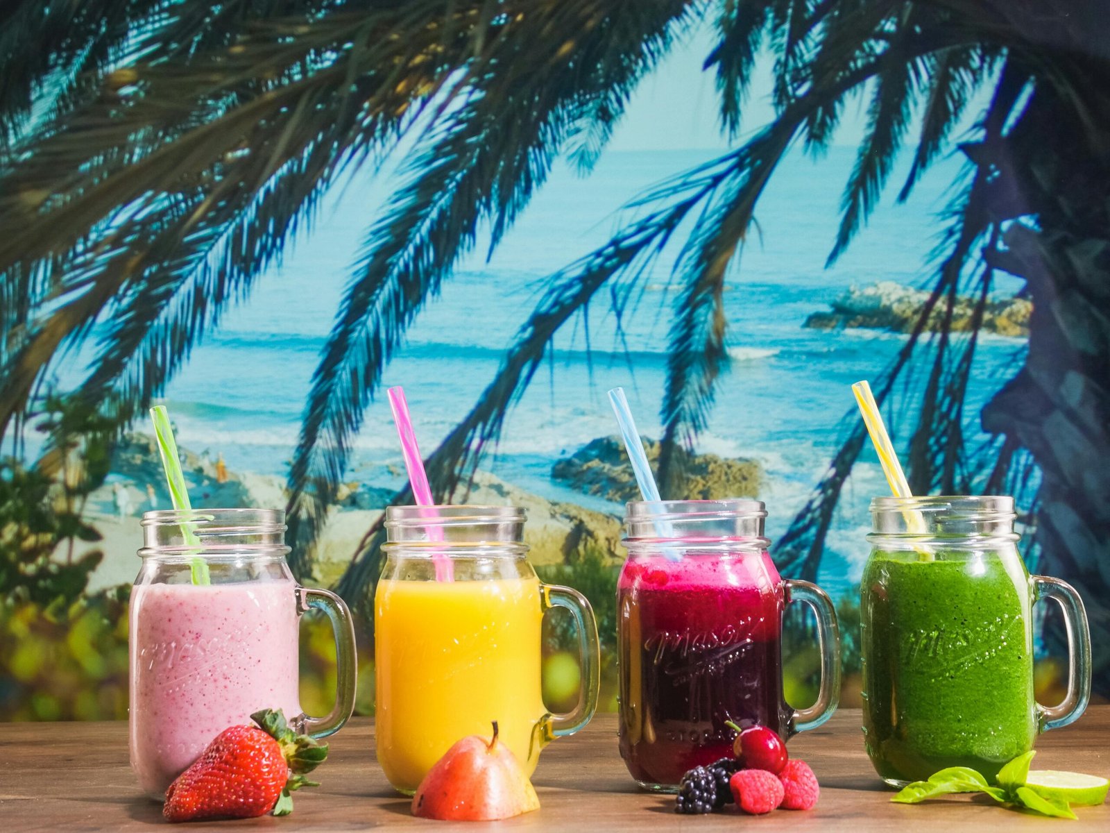 Colorful smoothies in mason jars with a tropical beach backdrop, perfect for summer vibes.